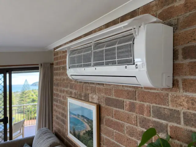 Clean split system with open front panel and visible filters on a brick wall in a coastal living room in Burleigh Heads