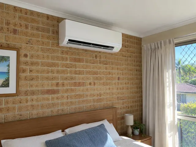 Clean split system mounted high on a brick bedroom wall above a bed in a home in Palm Beach
