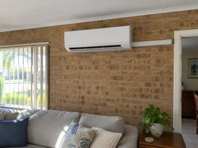 Wall-mounted split system on a brick living room wall above a sofa in Burleigh Waters
